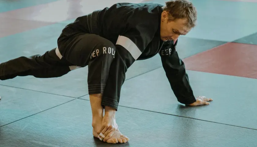 Mężczyzna w czarnym kimonie wykonuje rozciąganie. To część jego planu treningowego pod sporty walki, przygotowującego ciało do dynamicznych ruchów.