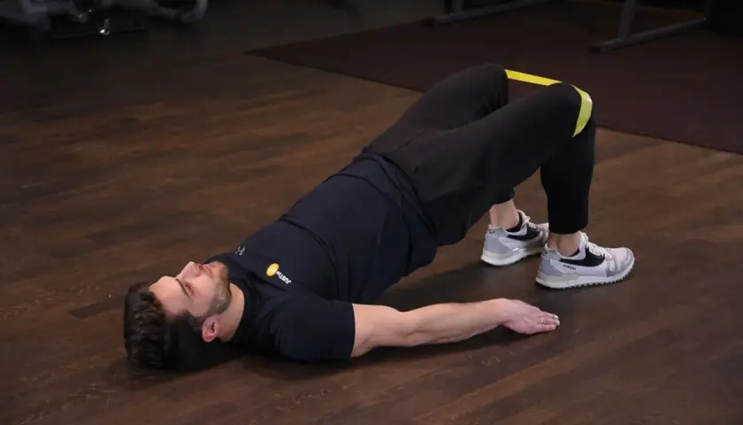 Mężczyzna wykonuje ćwiczenie glute bridge z gumą na udach, napinając pośladki.
