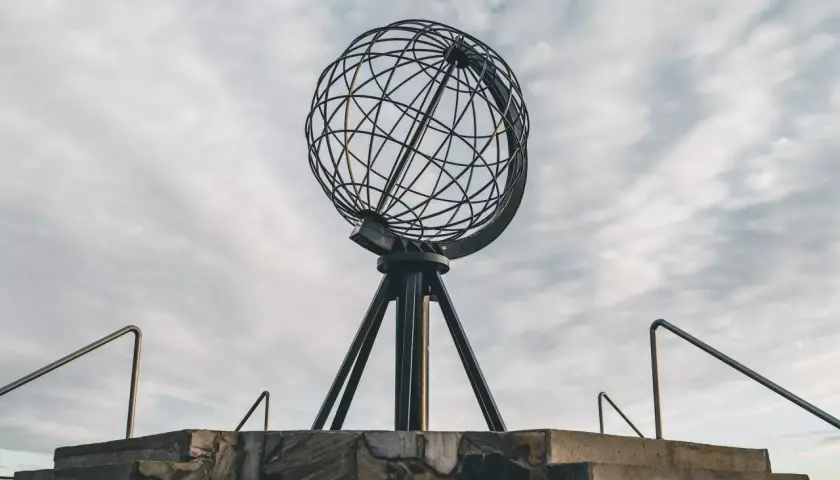 Metalowy glob na statywie na tle pochmurnego nieba, widok z dołu.
