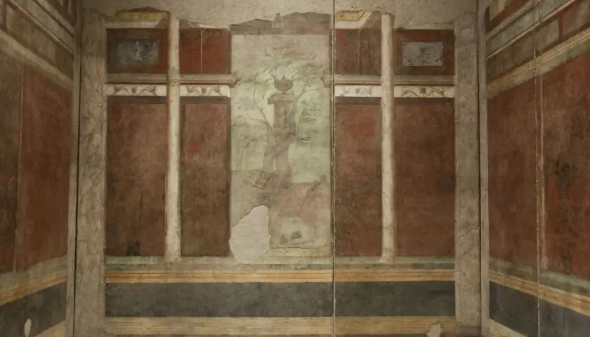 Affresco nella casa di Livia: colonne, pannelli rossi e un paesaggio centrale con un albero e un vaso.