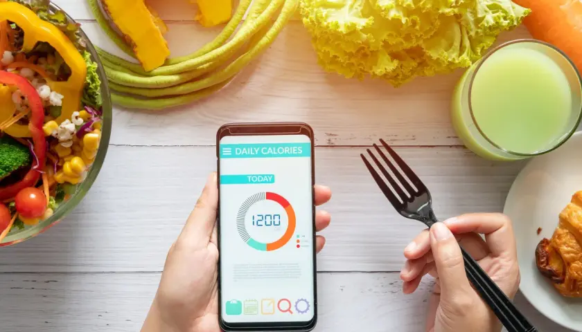 Aplikacja pokazuje dzienne zapotrzebowanie kaloryczne 1200 kcal. Obok sałatka, sok i rogalik.
