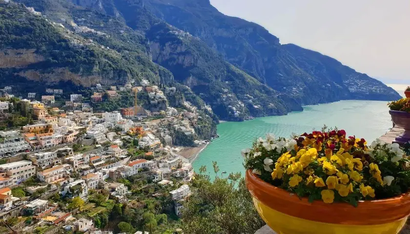 Colorful flowers bloom overlooking Positano, a stunning town cascading down the cliffs. This view offers inspiration for where to stay in Amalfi Coast.