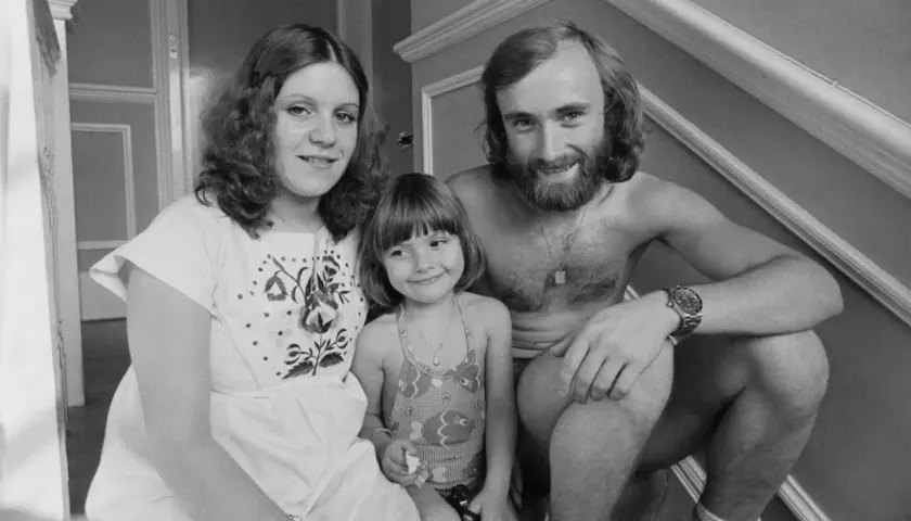 Phil Collins z żoną i córką, uśmiechnięci, siedzą na schodach.