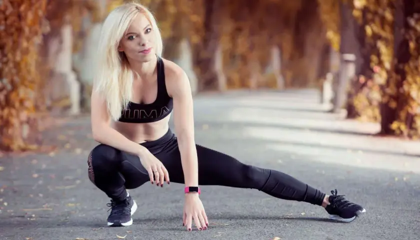 Blondynka w sportowym stroju wykonuje ćwiczenia rozciągające. Jej trening spinningowy jest gotowy do rozpoczęcia w jesiennej alei.