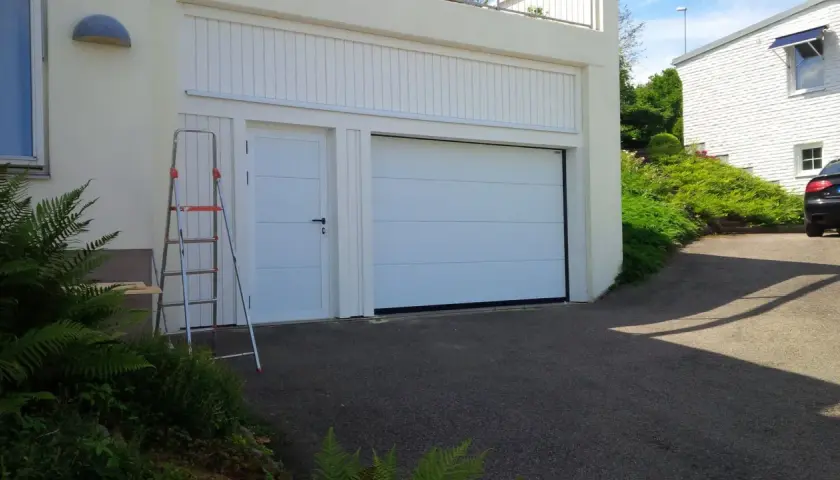En vit garageport montering pågår. En stege står bredvid, redo för nästa steg.