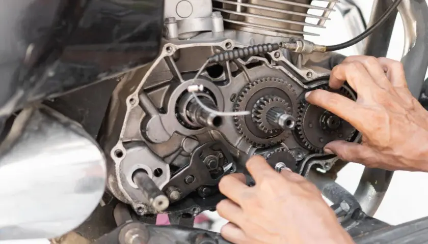 Mani che lavorano sul motore di una moto, ingranaggi visibili. Possibili cause di perdita potenza motore diesel.