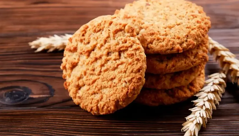 Biscotti integrali da colazione dorati e croccanti, impilati su un tavolo di legno scuro, con spighe di grano a lato.