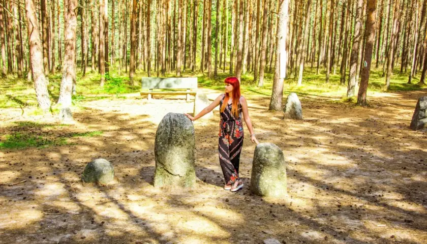Kobieta z rudymi włosami stoi między kamieniami w lesie.