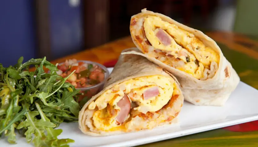 Pyszny omlet z tortillą, jajecznica, szynka i ziemniaki zawinięte w placek. Obok sałatka i salsa.