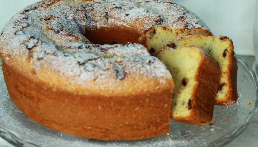 Ciambellone allo yogurt soffice e profumato, cosparso di zucchero a velo e gocce di cioccolato. Perfetto per la colazione o la merenda.