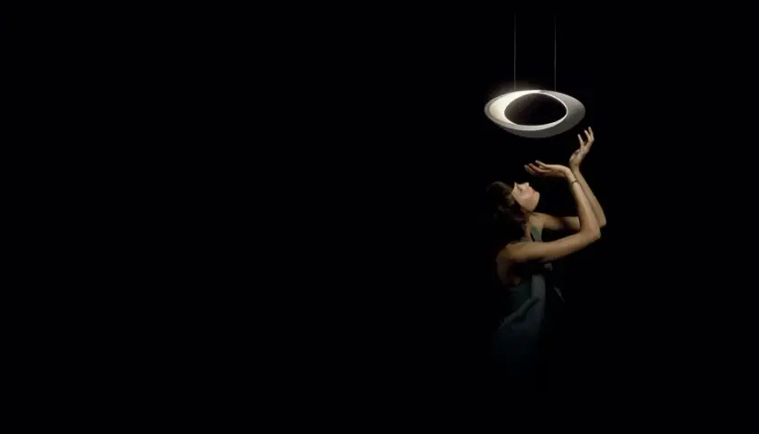 Kobieta wyciąga ręce do nowoczesnej lampy wiszącej, która wygląda jak pierścień. Skracanie lampy wiszącej pozwala na stworzenie intymnej atmosfery.