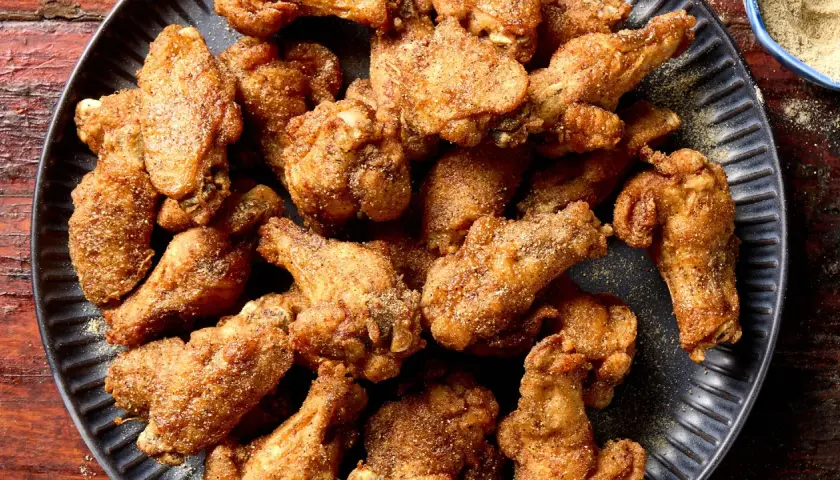 A pile of crispy, golden-brown Nagoya style chicken wings, seasoned with spices, on a dark plate.