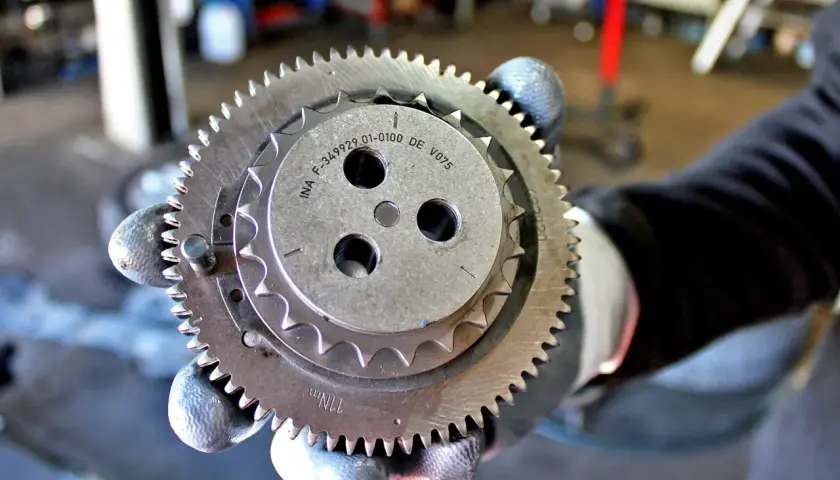 Zużyty łańcuch rozrządu objawia się wyślizganymi zębami koła. Mechanik pokazuje element z widocznymi śladami zużycia.