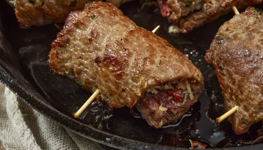 Involtini di carne in padella con sughetto, ripieni e cotti a puntino, pronti per essere gustati.