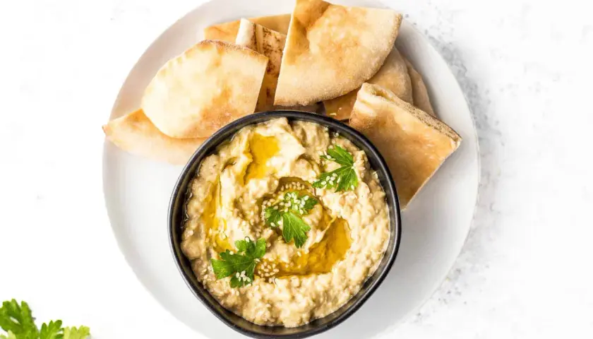 Un bol de caviar d'aubergine crémeux, garni d'huile d'olive, de persil et de sésame, servi avec des morceaux de pain pita.