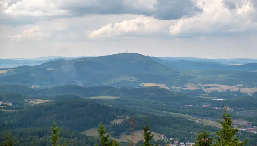 Widok na rozległą, zieloną dolinę z dominującą, zalesioną borową górą na horyzoncie. Na szczycie góry widoczna wieża telekomunikacyjna.