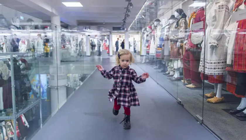 Mała dziewczynka biega po muzeum dla dzieci im. Janusza Korczaka, mijając gabloty z tradycyjnymi strojami.