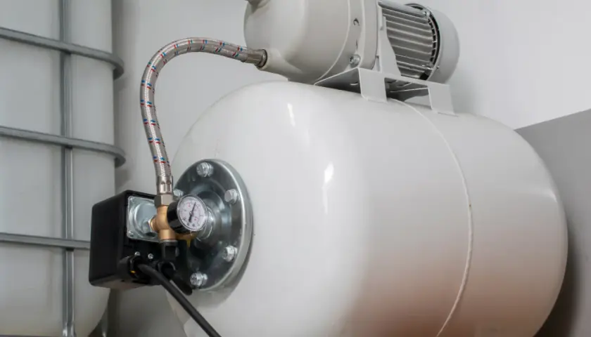 Biały zbiornik hydroforowy z manometrem i wężem. Może to oznaczać, że hydrofor często się włącza.