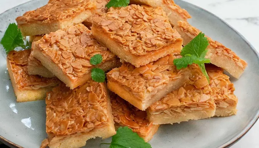 En hög med fyrkantiga bitar av en härlig mandelkaka, perfekt för ett "baka i långpanna deluxe recept". Garnerad med mynta.