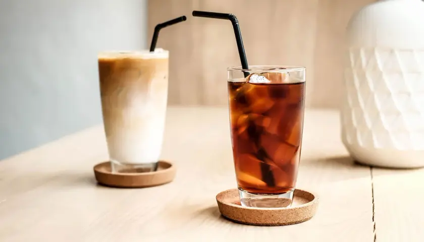 Zwei Gläser mit Eiswürfeln und Strohhalmen. Eines ist ein cremiger Eiskaffee, das andere ein dunkler Kaffee mit kaltem Wasser.