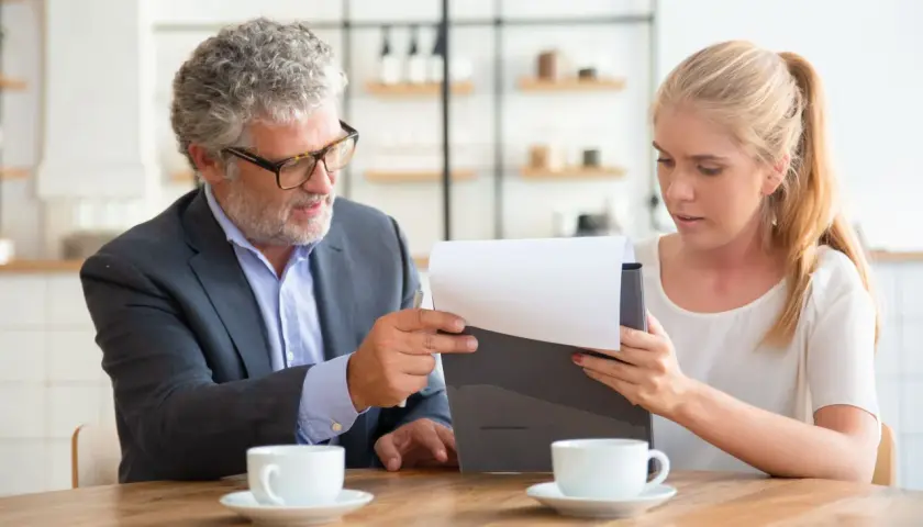 Hombre y mujer revisan documentos. Él explica que un precontrato es vinculante. Tazas de café en la mesa.