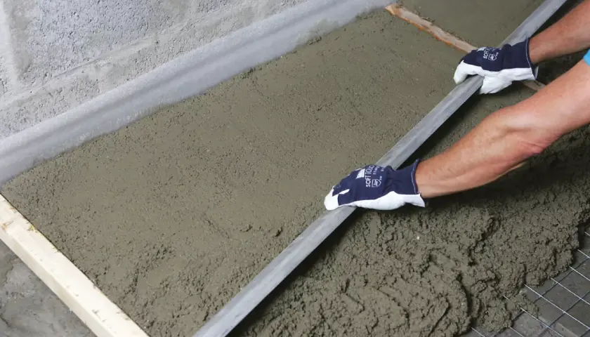 Ręce w rękawiczkach wyrównują świeżą wylewkę za pomocą łaty.