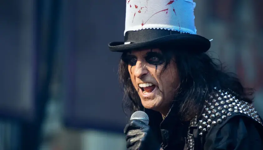 Alice Cooper w Polsce, w swoim charakterystycznym makijażu i z kapeluszem, śpiewa do mikrofonu.