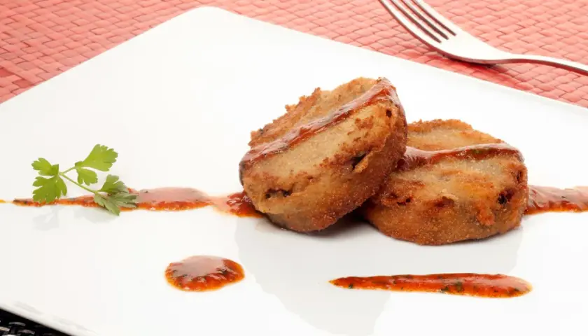 Dos manitas de cerdo rebozadas y fritas, servidas con salsa roja y perejil en un plato blanco.