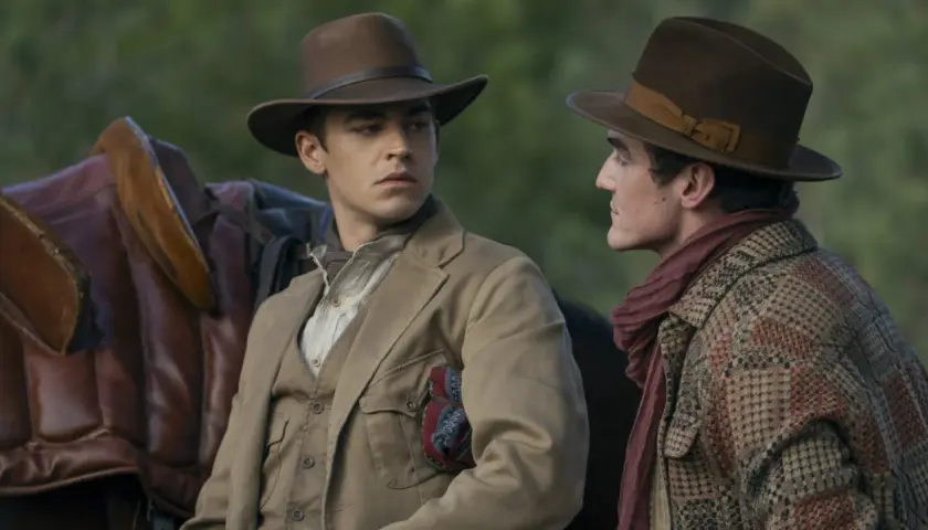 Två unga män i hattar och tidstypiska kläder, en med en sadel bredvid sig. Kanske en ung Sherlock Holmes på ett äventyr.