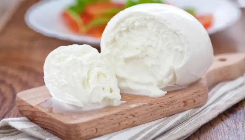 Świeża kulka mozzarelli na desce, w tle sałatka. Zastanawiasz się, ile kcal ma kulka mozzarelli?