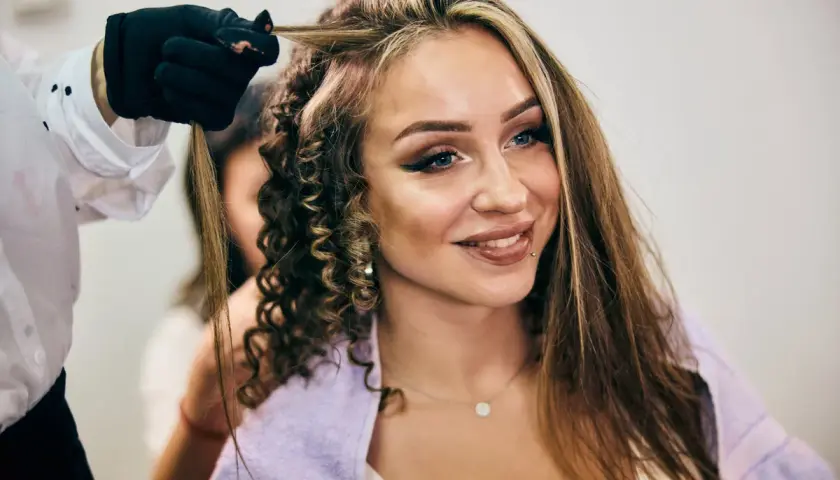 Stylist tworzy loki na włosach kobiety z widocznymi chunky highlights.
