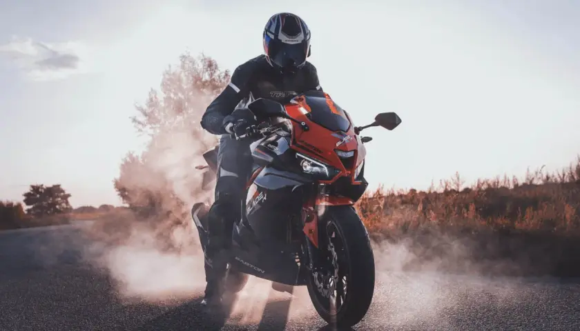 Motocyklista w kasku i kombinezonie na czerwono-czarnym motocyklu Barton Blade 125, unoszący kurz. Czy motocyklem 125 można jeździć po autostradzie?