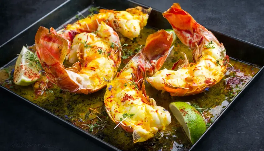 Langoustes grillées sur plancha, nappées d'une sauce verte et garnies de quartiers de citron vert et de thym.