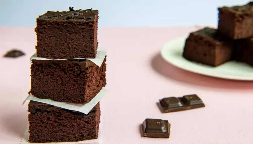 Ciemne, wilgotne brownie z fasoli ułożone w wieżę, obok kawałki czekolady.
