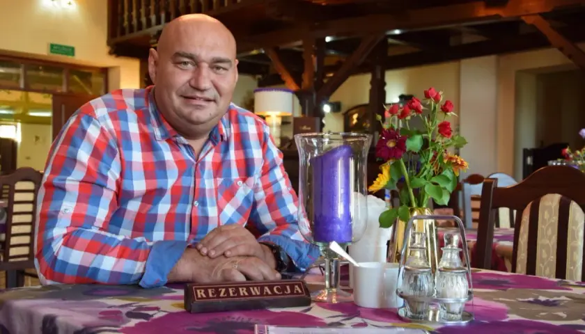 Łysy mężczyzna w kratę siedzi przy stole z kwiatami i świecą.
