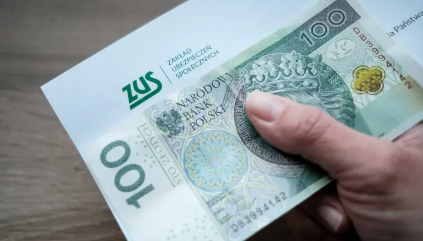 Dłoń trzyma banknot 100 zł i dokument ZUS. Może to symbolizować wsparcie finansowe, np. renta na depresję.