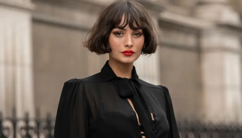 Eine Frau mit einem lässigen, **choppy bob** und rotem Lippenstift trägt eine transparente schwarze Bluse.