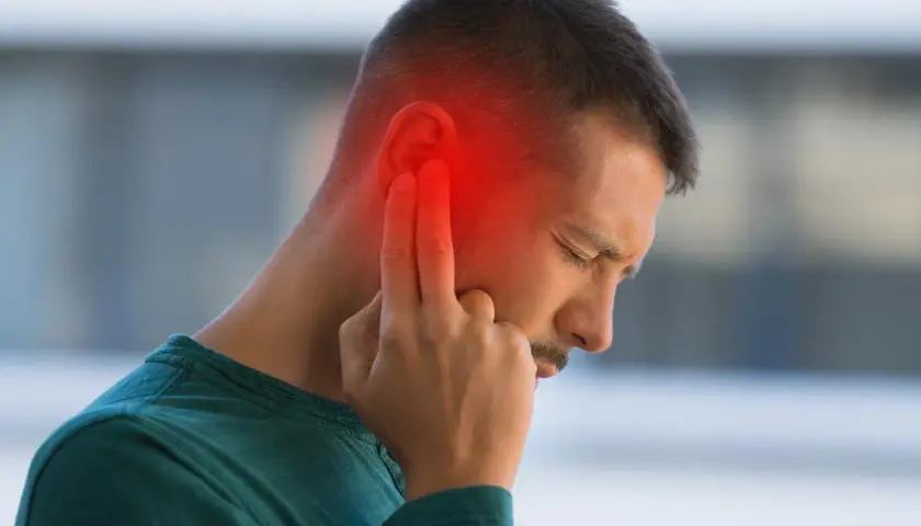 Hombre con dolor de oído, señalando la zona afectada con un halo rojo. Podrían ser sabañones en las orejas.