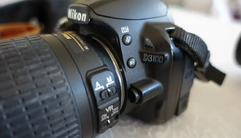 Zbliżenie na aparat Nikon D3100. Widoczny obiektyw z pierścieniem ostrości i przełącznikami AF/M oraz VR ON/OFF. D3100 to model, którego nikon d3100 dane techniczne warto poznać.