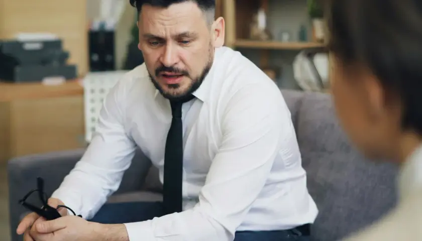 Mężczyzna w białej koszuli i krawacie, trzymający okulary, zastanawia się, jak inteligentnie zakończyć rozmowę.