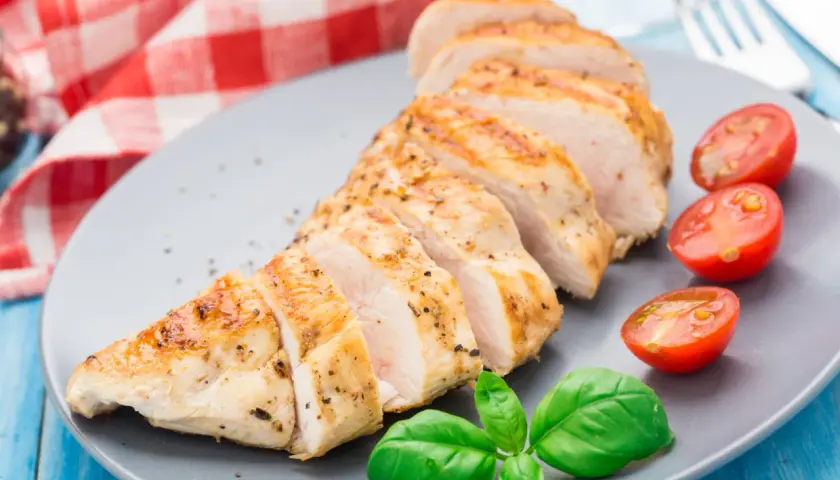 Tranches de blanc de poulet grillé, assaisonné de poivre et d'herbes, servi avec des tomates cerises et du basilic frais.