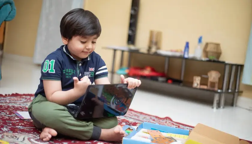 Mały chłopiec, mój syn, uczy się francuskiego przez tablet, siedząc na dywanie.