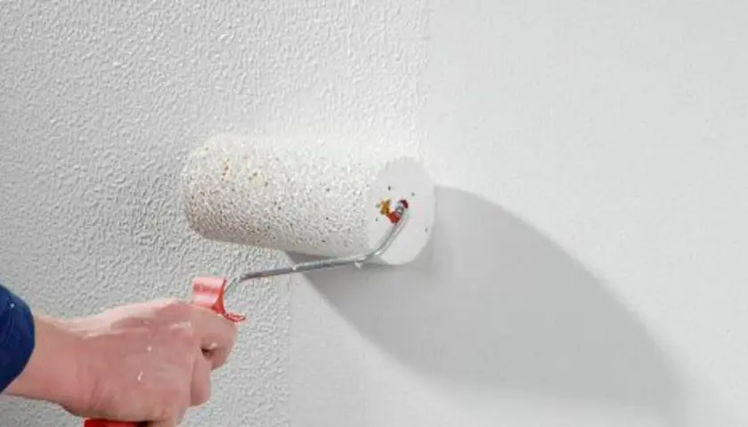 Eine Hand rollt mit einem Farbroller eine strukturierte Wand. Der Rollputz innen wird aufgetragen und verleiht der Oberfläche eine interessante Textur.