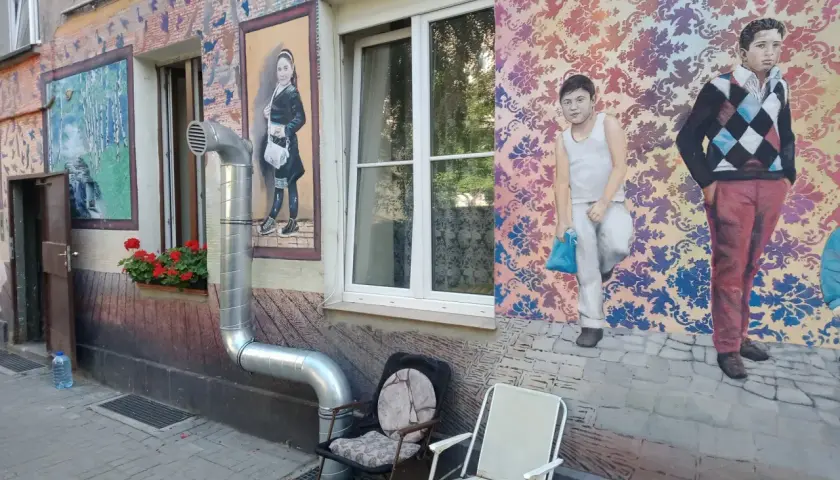 Kolorowe murale z postaciami dzieci i wzorami zdobią kamienicę na Nadodrzu. Dwa krzesła stoją przed ścianą.