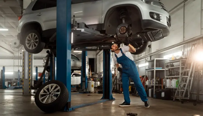 Mechanik w warsztacie samochodowym naprawia podniesiony samochód.