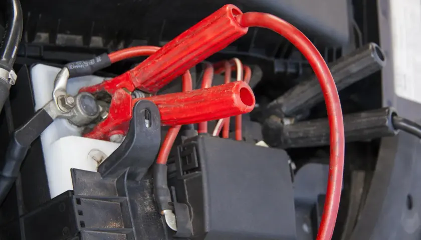 Czerwone kable rozruchowe podłączone do akumulatora. Zastanawiasz się, czy można odpalać auto przy podłączonym prostowniku?