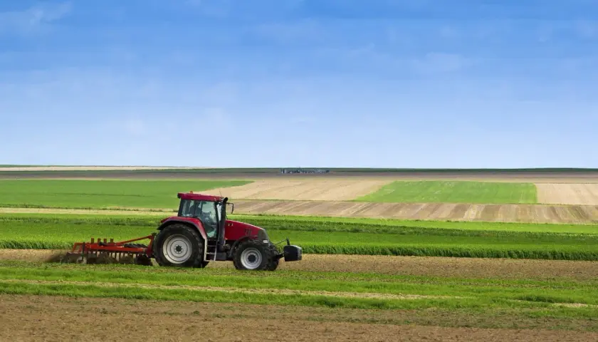 Tracteur rouge travaillant dans un champ, préparant le sol pour le semis direct. Paysage agricole sous un ciel bleu.