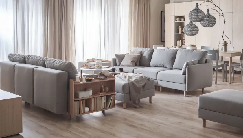 Przytulny salon inspiracje: szara sofa, drewniane meble, jasne zasłony i dekoracje tworzą ciepłą atmosferę.