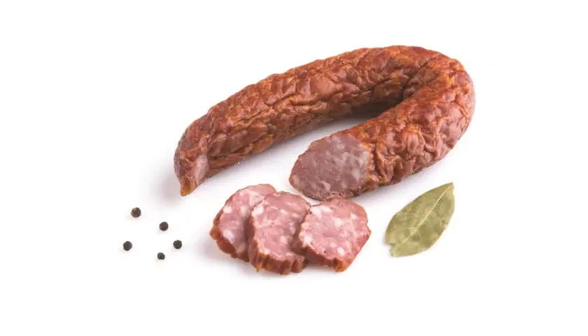 Kiełbasa jałowcowa w całości i w plasterkach, z ziarnami pieprzu i liściem laurowym.