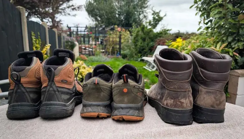 Choosing hiking boots: A selection of hiking boots and shoes, from lighter trail runners to sturdy leather boots, are lined up outdoors.